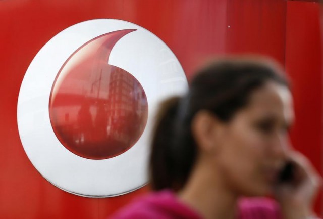 A woman talks on her mobile phone as she walks past a Vodafone store in London