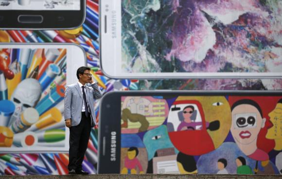A man uses his mobile phone in front of a giant advertisement promoting Samsung Electronics' new Galaxy S5 smartphone, at an art hall in central Seoul