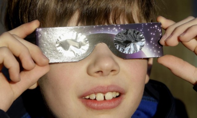 A boy looks at the sun through protective glasses in Berlin, Germany