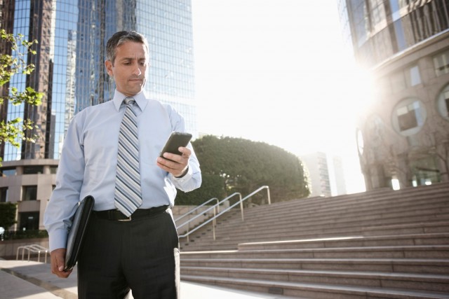 Los Angeles, California, USA --- Hispanic businessman text messaging on cell phone outdoors --- Image by © Peathegee Inc/Blend Images/Corbis
