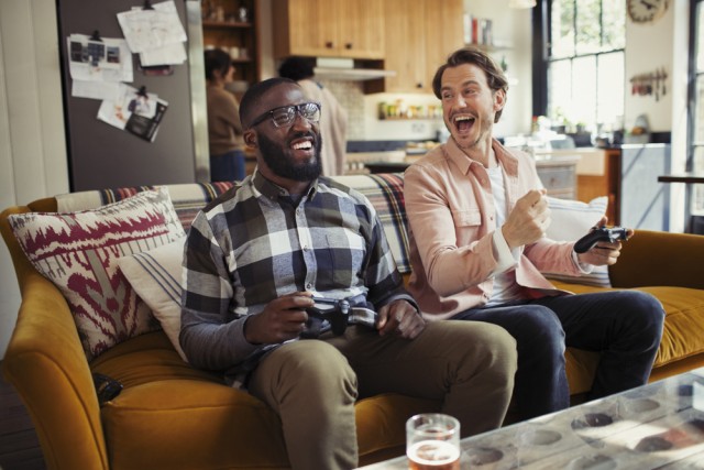 Laughing men friends playing video game on living room sofa