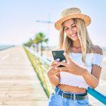 Young blonde tourist girl smiling happy using smartphone at the promenade.